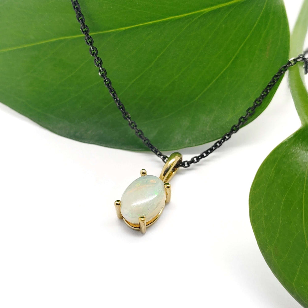 14kt yellow gold opal pendant with oval cabochon on black chain, styled with green leaves
