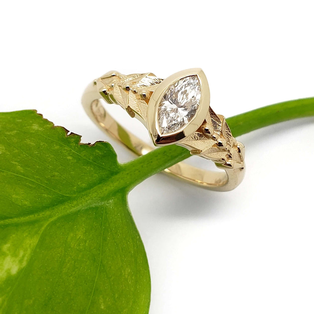 Oriana ring with marquise lab diamond in 14kt yellow gold, leaf motif, beside a green leaf