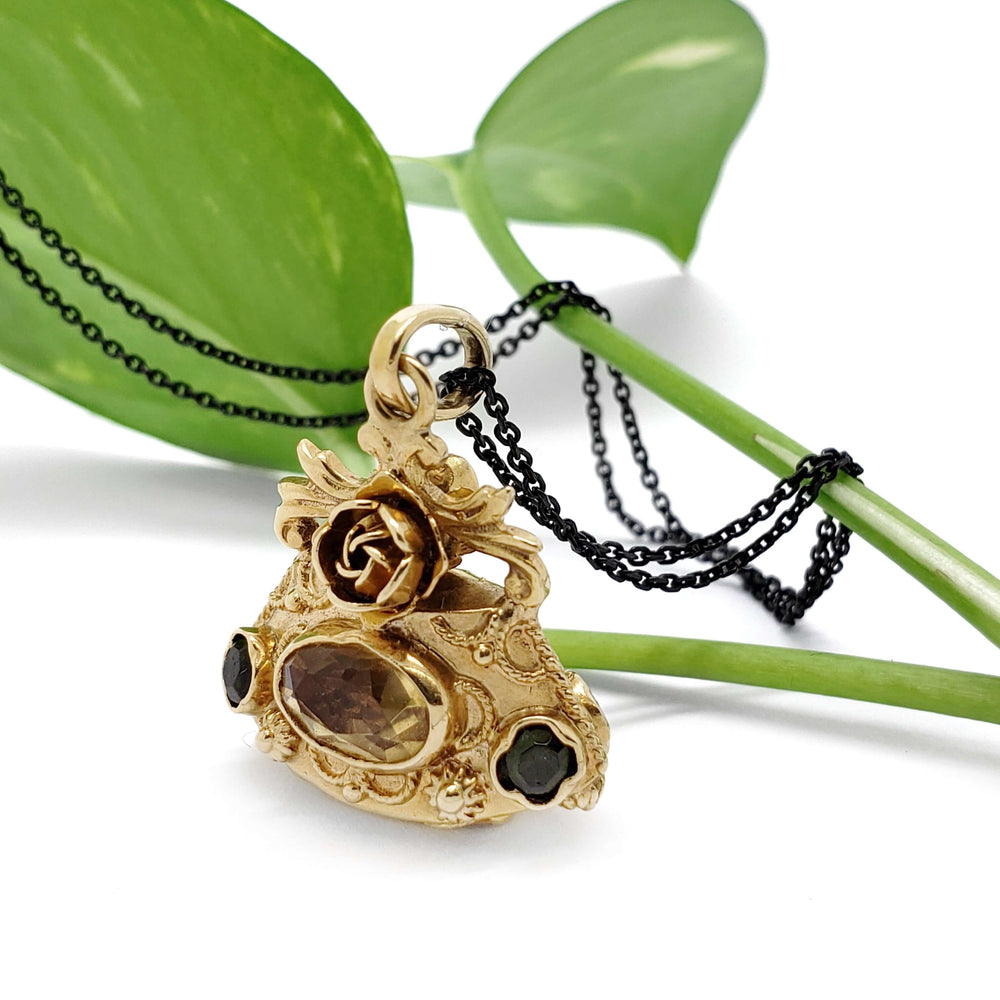 Ornate 18kt yellow gold fob pendant with citrine and peridot, displayed with green leaves