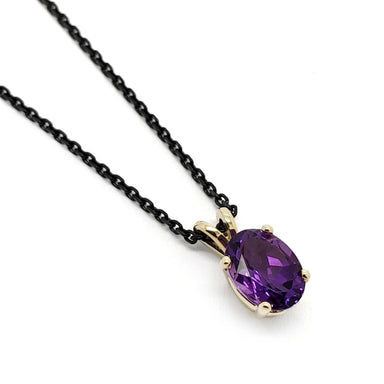 Oval amethyst pendant in 14kt yellow gold on black chain, close-up on white background