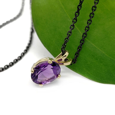Side view of oval amethyst pendant in 14kt yellow gold on black chain, with green leaf