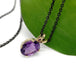 Side view of oval amethyst pendant in 14kt yellow gold on black chain, with green leaf