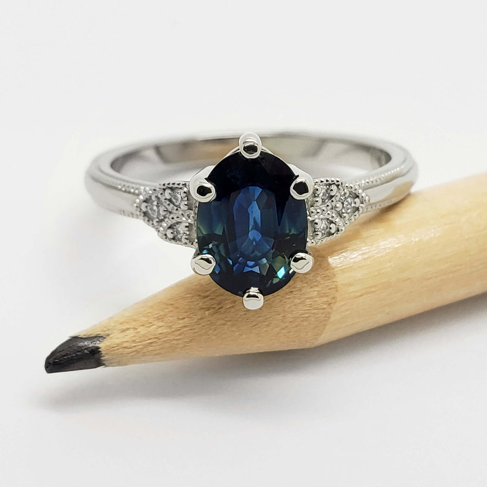 Oval blue sapphire and diamond white gold ring shown beside a pencil for scale