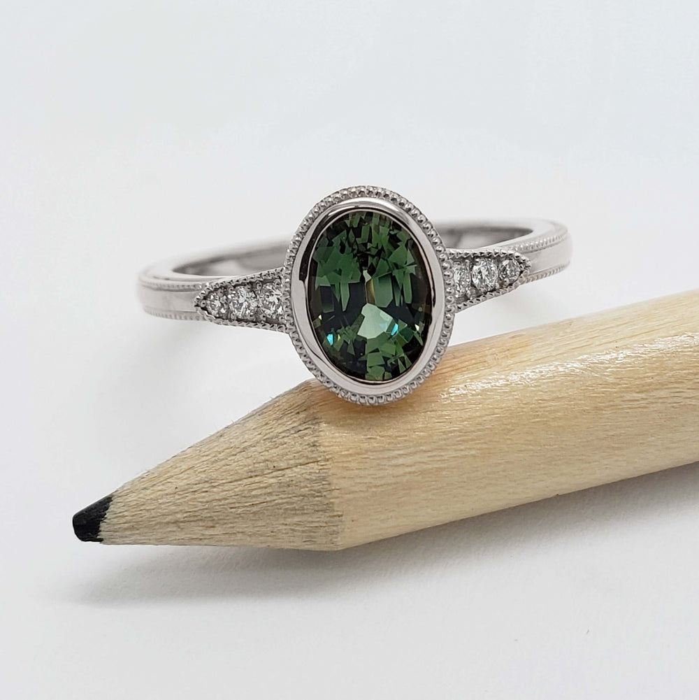 Oval green Australian sapphire and diamond ring in white gold, shown balanced on a pencil