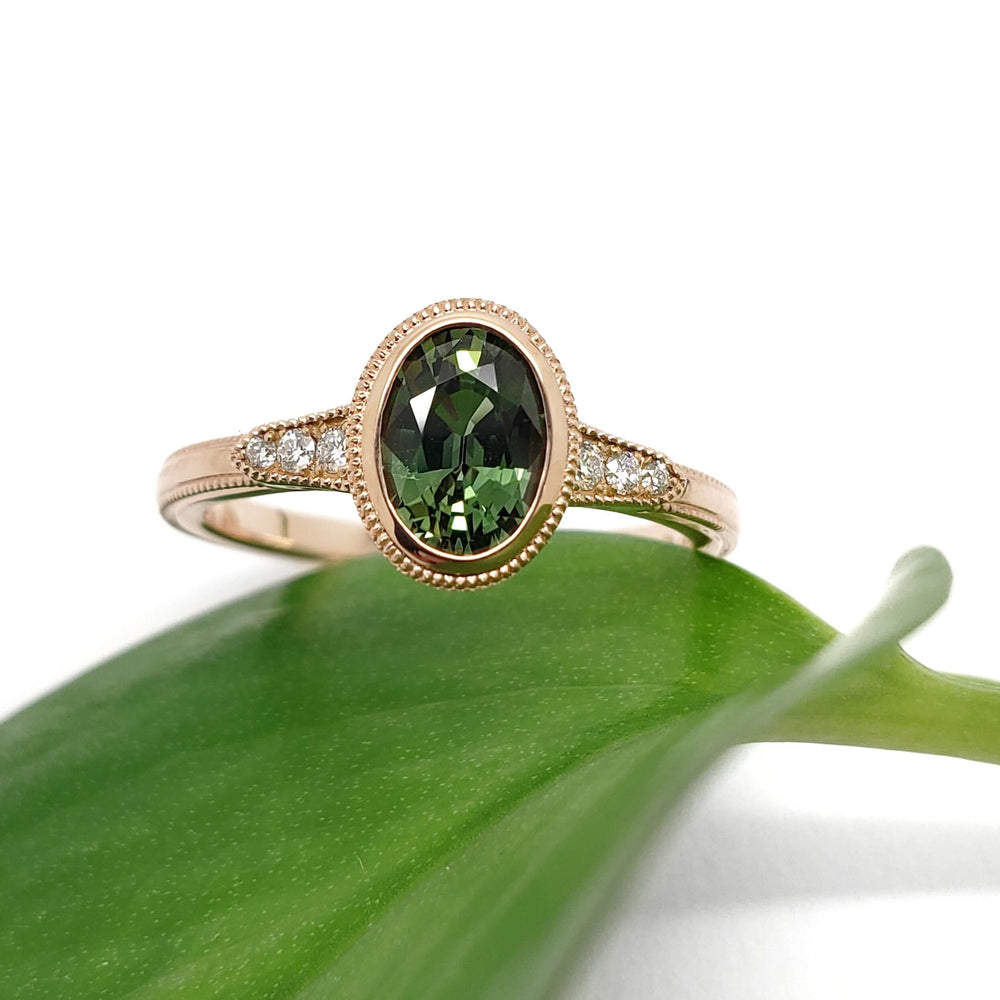 Oval green sapphire and Canadian diamond ring in rose gold resting on a green leaf