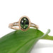 Oval green sapphire and Canadian diamond ring in rose gold resting on a green leaf