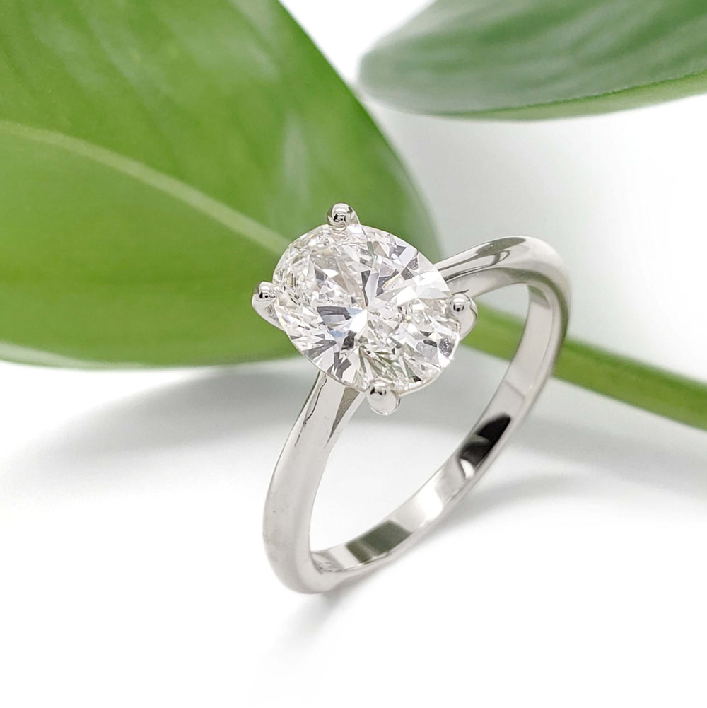 Oval lab diamond engagement ring in 14kt white gold, shown with green leaves