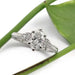 Oval lab diamond engagement ring in white gold with vintage-inspired accents, beside a green leaf