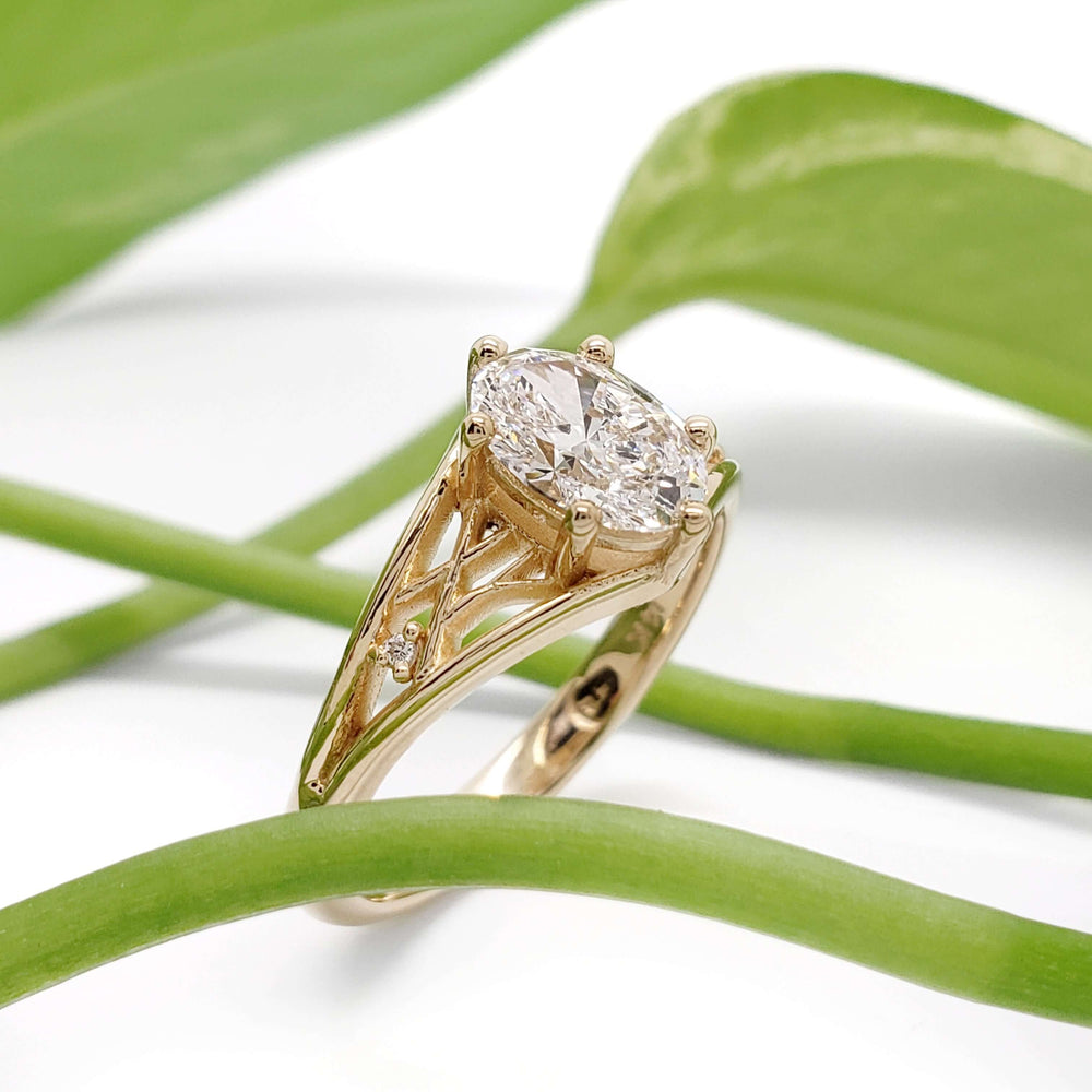 Oval lab diamond ring in 14kt yellow gold with lattice setting, shown with green leaves