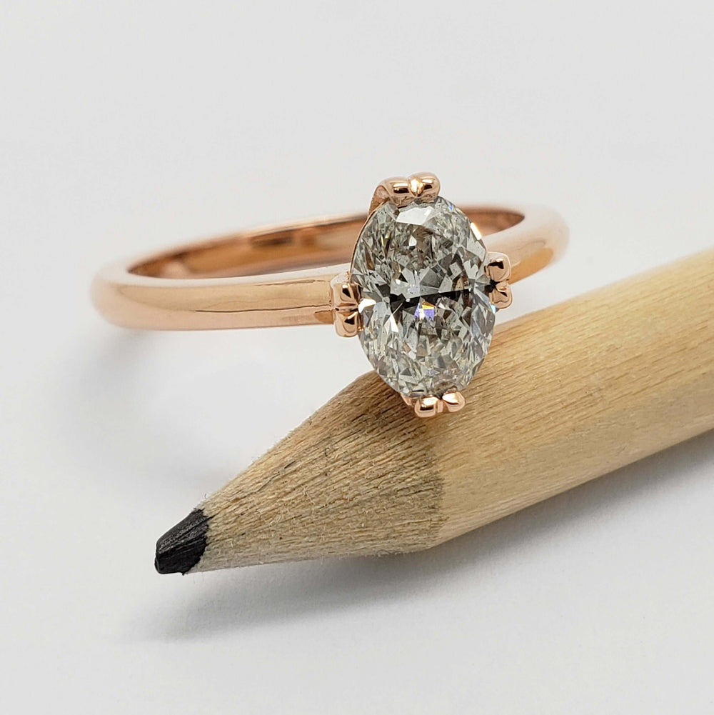 Oval lab-grown diamond solitaire ring in rose gold, shown resting on a pencil