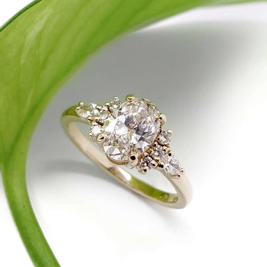 Oval lab grown diamond cluster ring in 14kt yellow gold, displayed on white with green leaf