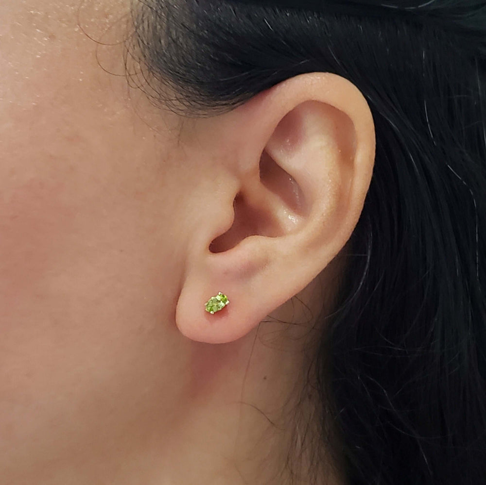 Oval green peridot stud earring in 14kt yellow gold worn on ear