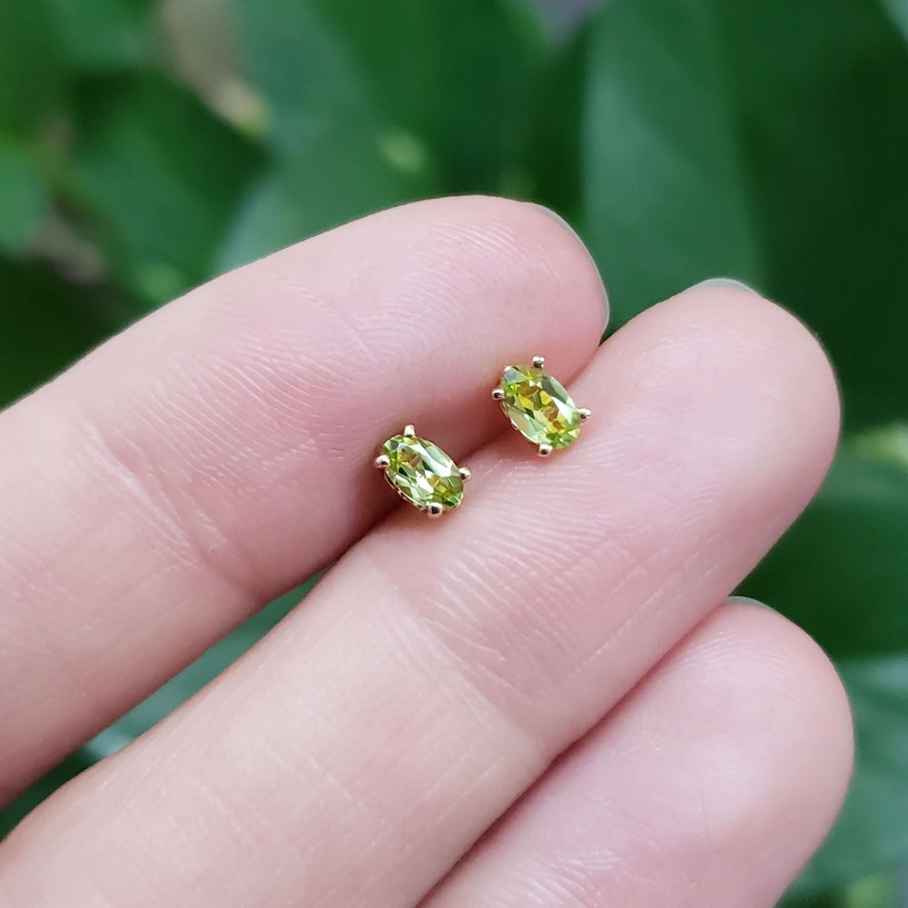 Hand holding oval cut green peridot stud earrings in 14kt yellow gold