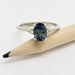 Oval teal Australian sapphire and lab diamond ring in white gold, beside a pencil
