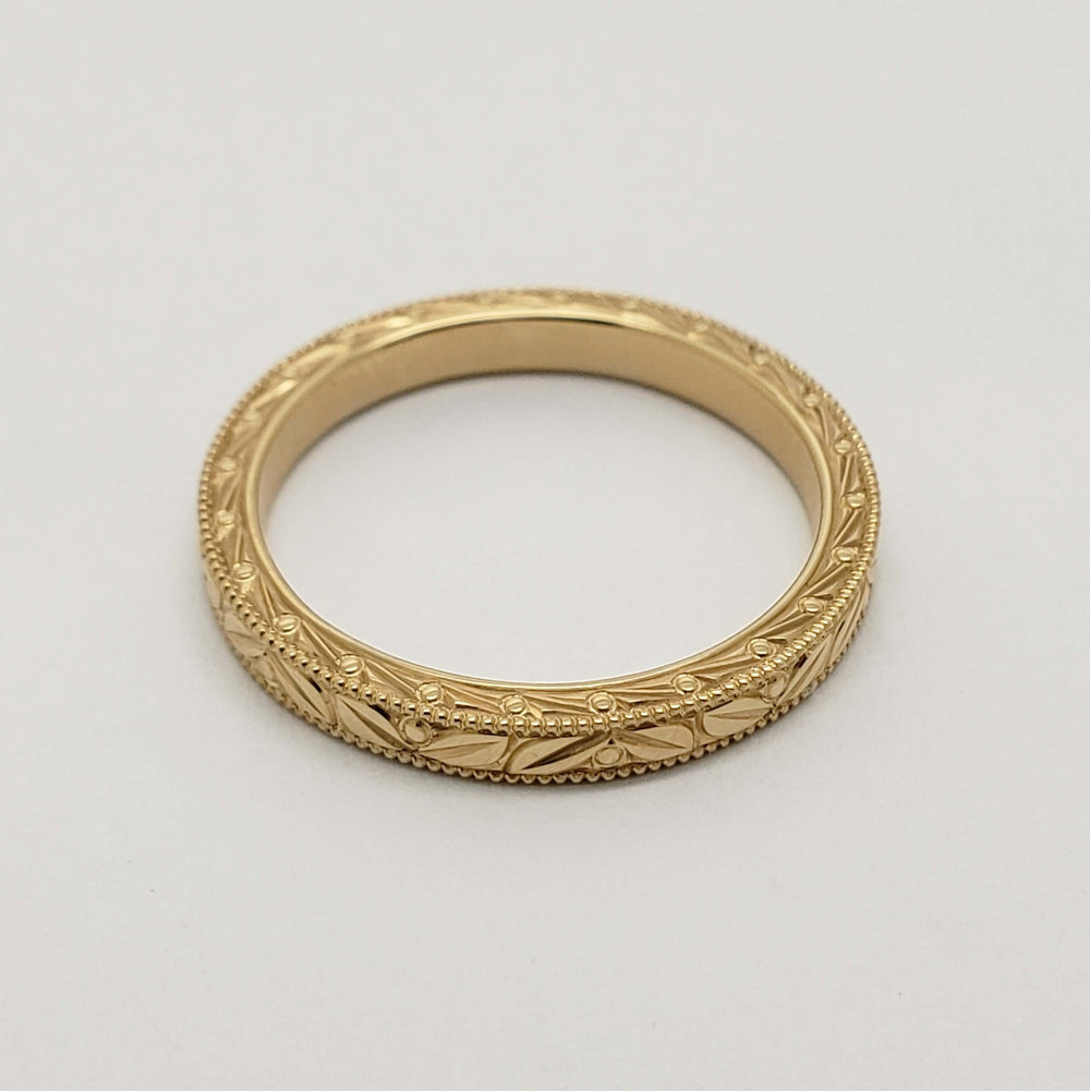 Overhead view of 14kt yellow gold wedding ring with detailed Salal engraving and millgrain edge