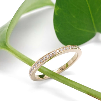 Pave-set Canadian diamond wedding ring in 14kt yellow gold beside a green leaf
