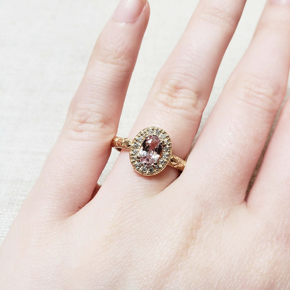 14kt yellow gold peach sapphire and diamond halo engagement ring worn on hand, floral engraved band