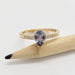 Pear-cut lavender sapphire and diamond ring in yellow gold beside a pencil