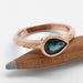 Pear-shaped teal sapphire ring in rose gold with engraved band, resting on pencil