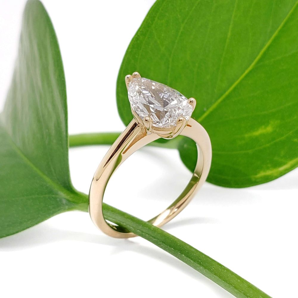 Pear lab diamond engagement ring in yellow gold displayed on green leaf