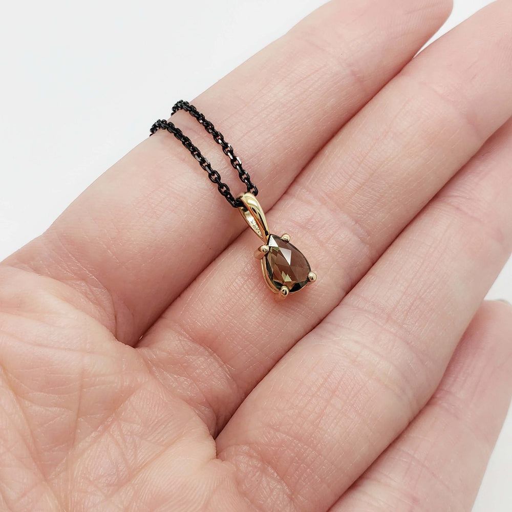 Pear rose cut green sapphire pendant in 14k yellow gold on black chain shown in hand