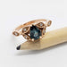 Pear teal sapphire and diamond leaf ring in 14k rose gold, displayed on a pencil