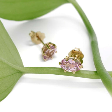 Pink imperial topaz and 14kt yellow gold stud earrings resting on a green leaf