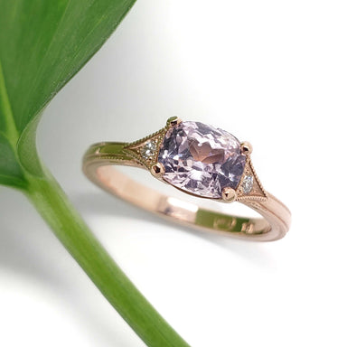 Pink sapphire and diamond engagement ring in rose gold beside a green leaf