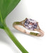 Pink sapphire and diamond engagement ring in rose gold beside a green leaf