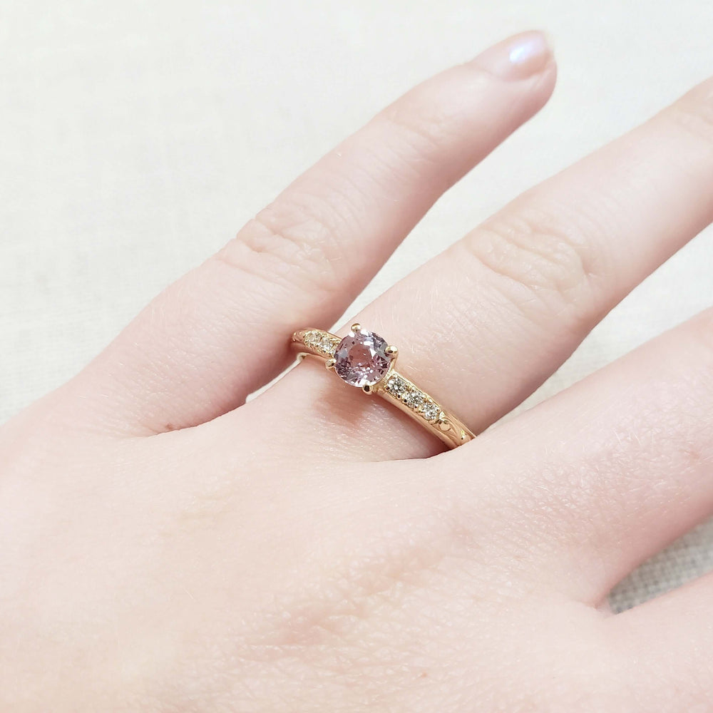 Pink sapphire and diamond engagement ring in yellow gold shown on hand