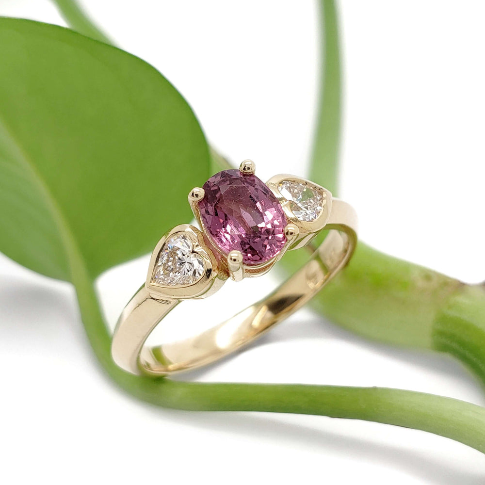 Pink sapphire and lab diamond engagement ring in yellow gold, shown with green leaves