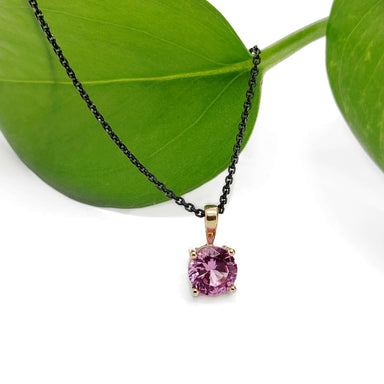Pink spinel pendant in 14kt yellow gold on black chain, displayed with green leaf
