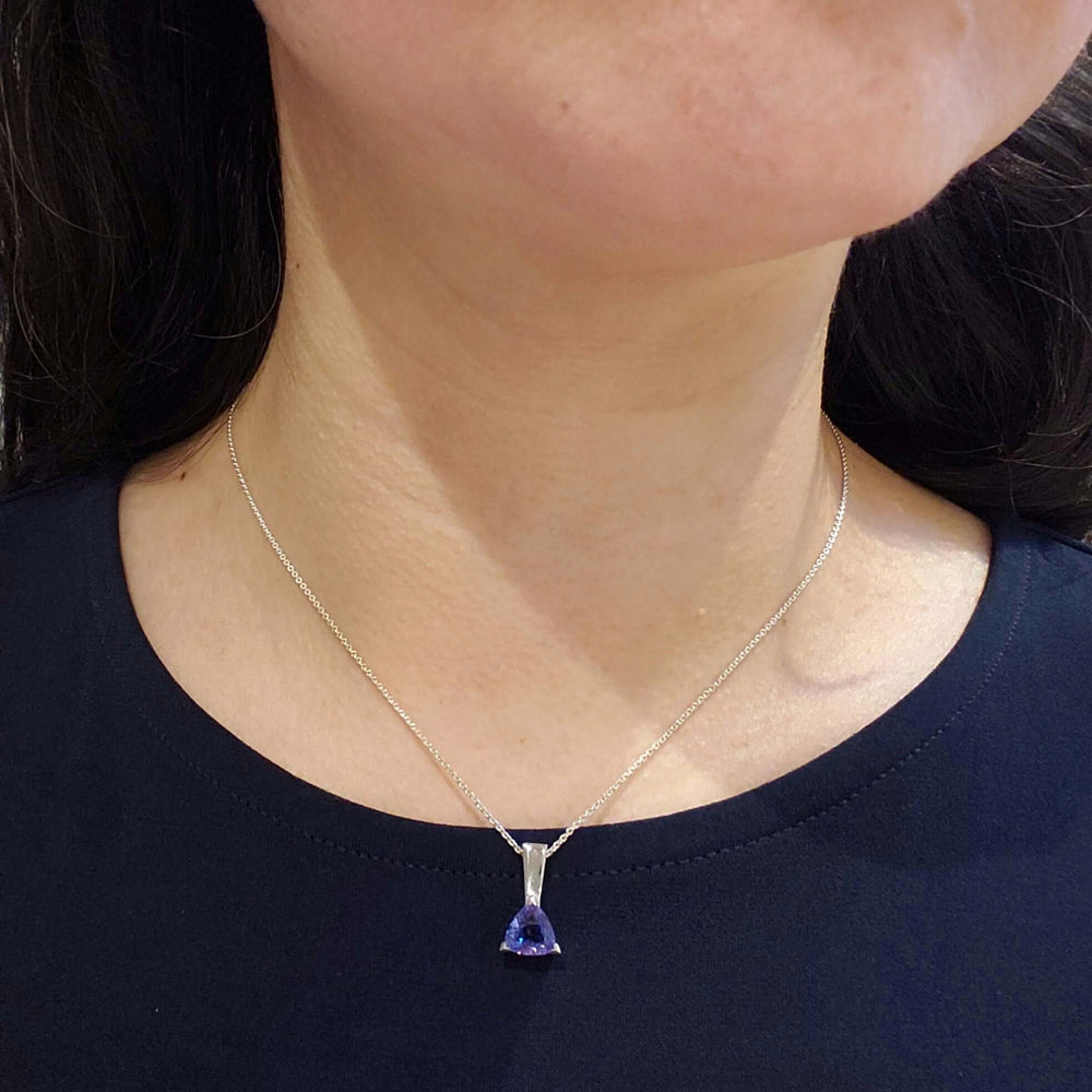 Platinum trilliant tanzanite pendant worn on a model, close-up on neck