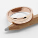 Polished 14kt rose gold wedding ring resting on a wooden pencil