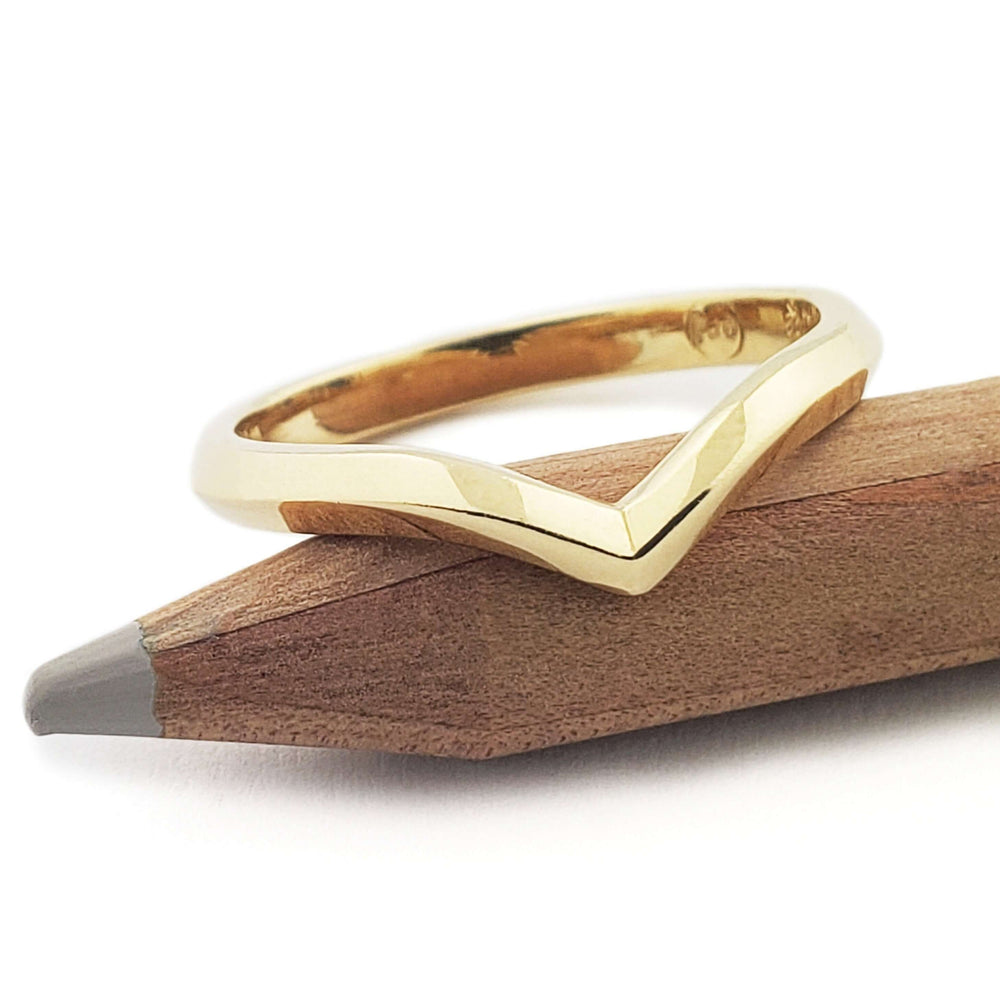 Polished 14kt yellow gold chevron wedding ring displayed on a pencil