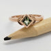 Princess cut green sapphire ring in rose gold with leaf accents, resting on a pencil