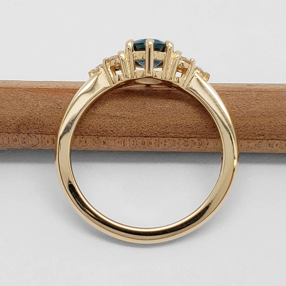 Profile view of 14k yellow gold Montana sapphire and diamond ring on a pencil