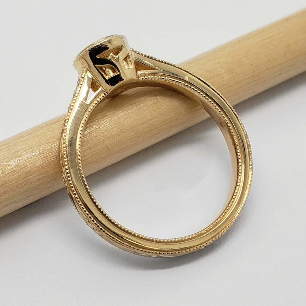 Profile of 14kt yellow gold engagement ring with millgrain and hand engraving, on pencil