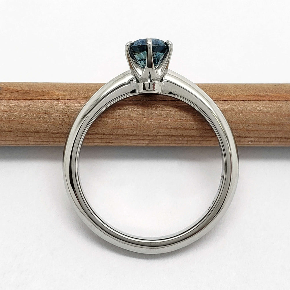 Profile view of white gold solitaire ring with blue Montana sapphire on a pencil