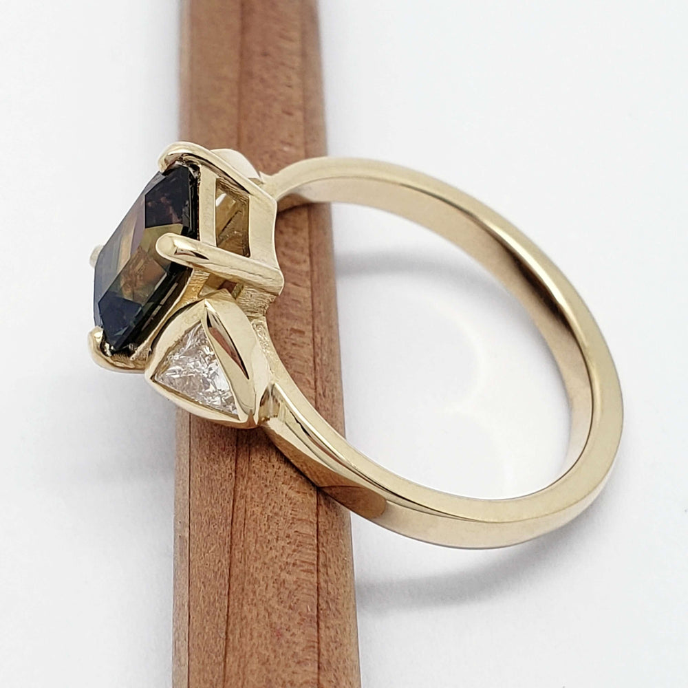Profile view of 14kt yellow gold ring with emerald cut sapphire and trillion diamonds