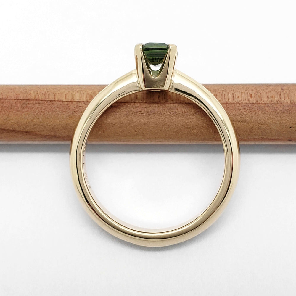 Profile view of 14kt yellow gold ring with green Tanzanian sapphire, band resting on pencil