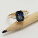 Radiant cut blue sapphire and pear lab diamond ring in yellow gold, displayed on a pencil
