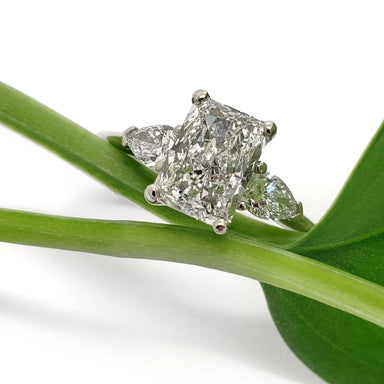 Radiant cut lab diamond three-stone ring in white gold resting on a green plant stem