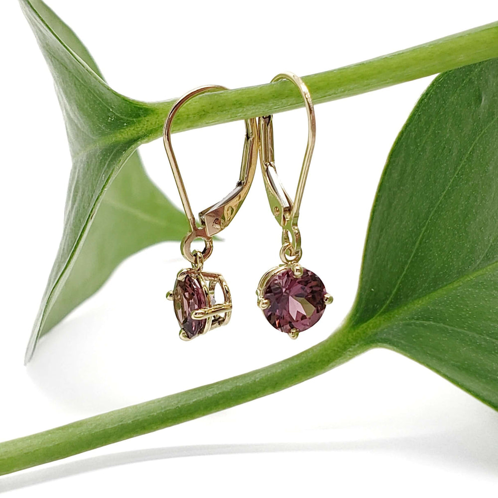 14kt yellow gold rhodolite garnet drop earrings displayed on a green leaf