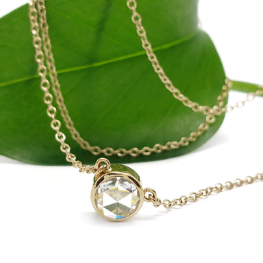Bezel-set rose cut moissanite necklace in 14kt yellow gold displayed on a leaf