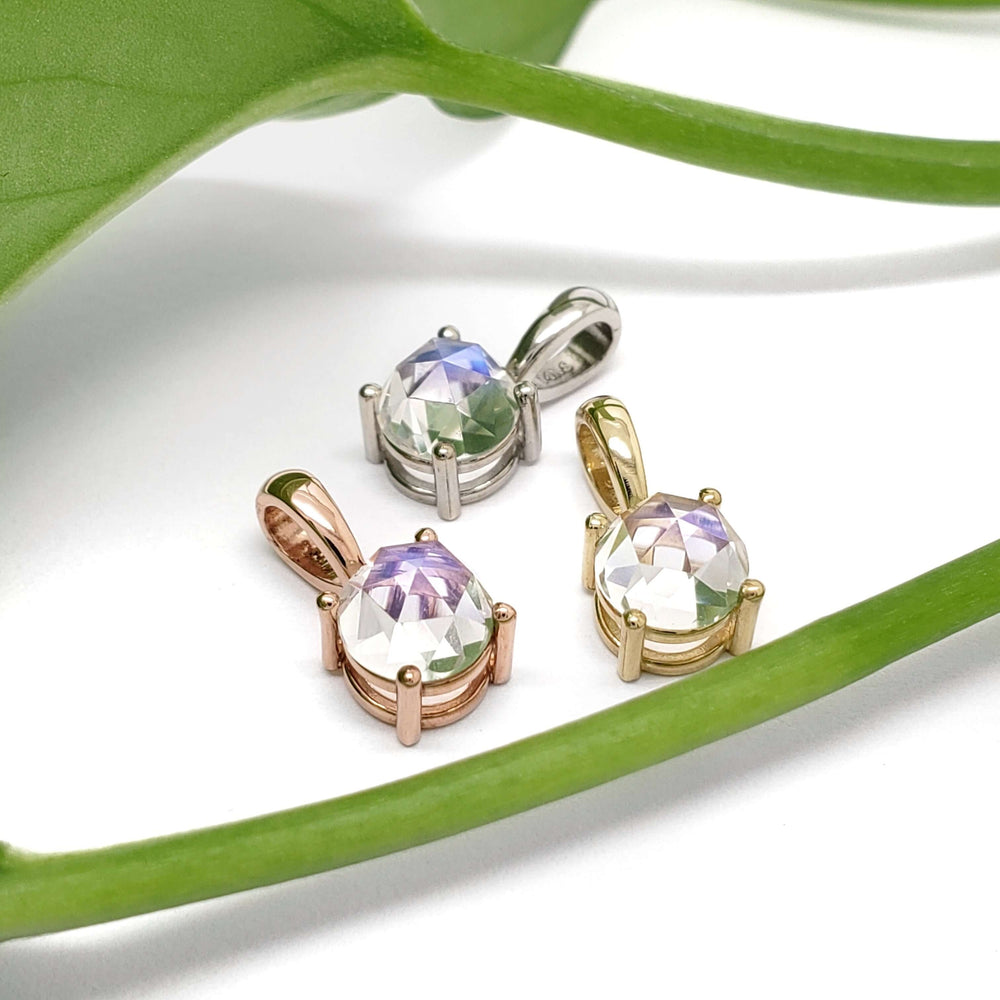 Rose cut moonstone pendants in yellow, rose, and white 14kt gold displayed with green leaf