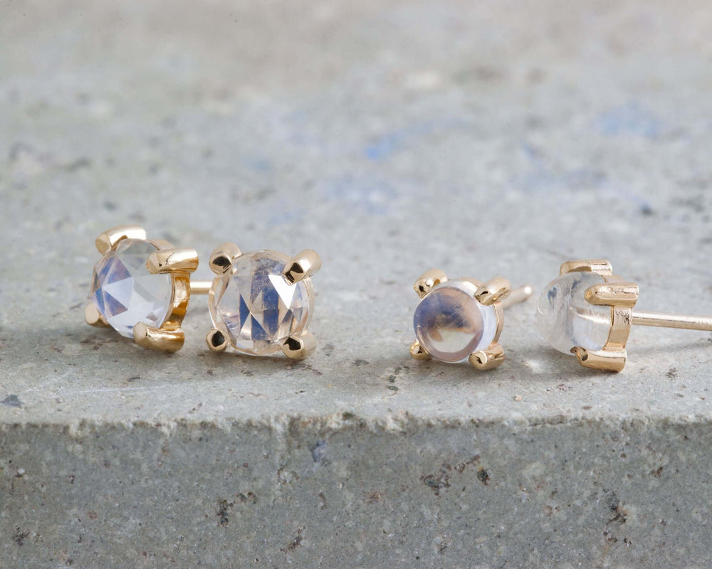 Rose cut moonstone stud earrings in 14kt yellow gold, two sizes, on stone surface