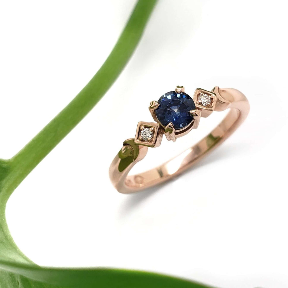 Handcrafted rose gold ring with blue Montana sapphire and diamond accents, styled with a green leaf