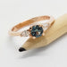 Rose gold ring with teal Montana sapphire and pear cut lab diamonds, shown on a pencil