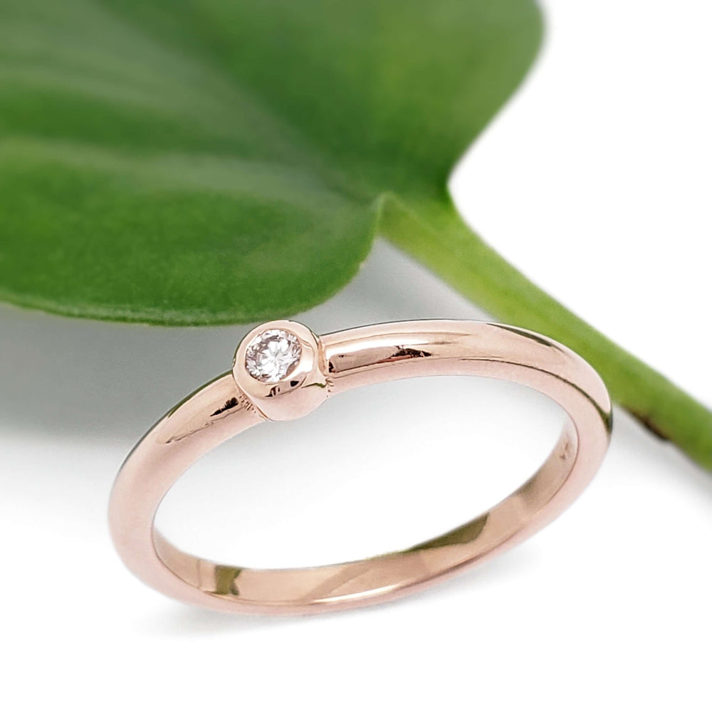 14kt rose gold bezel set diamond ring beside a green leaf